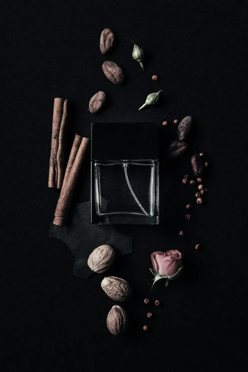 A perfume bottle surrounded by spices and roses on a dark background